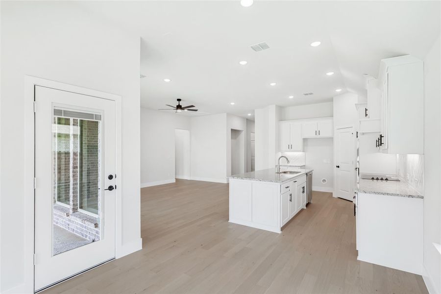 Open-concept kitchen with white cabinets, granite island, and light hardwood floors leading to living area