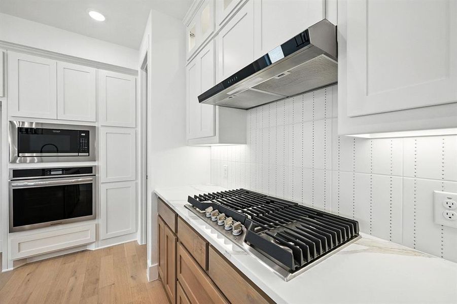 Kitchen featuring white cabinetry, appliances with stainless steel finishes, light wood-style flooring, wall chimney exhaust hood, and recessed lighting Kitchen featuring white cabinetry, appliances with stainless steel finishes, light wood-style flooring, wall chimney exhaust hood, and recessed lighting