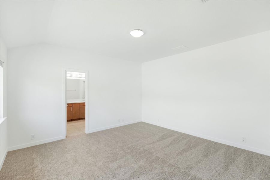 Empty bedroom with beige carpet and white walls, with ensuite bathroom visible through doorway