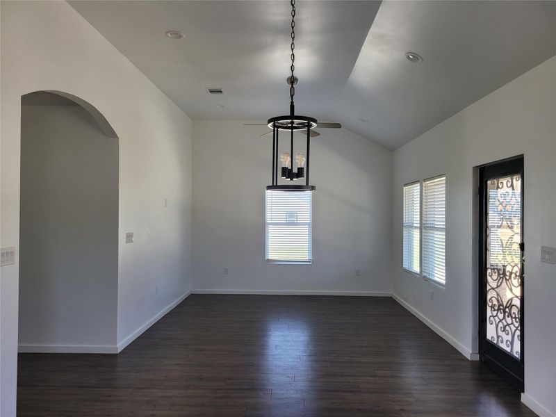 An open concept living area boasts vaulted ceilings and dark wood flooring, illuminated by natural light and recessed lighting.