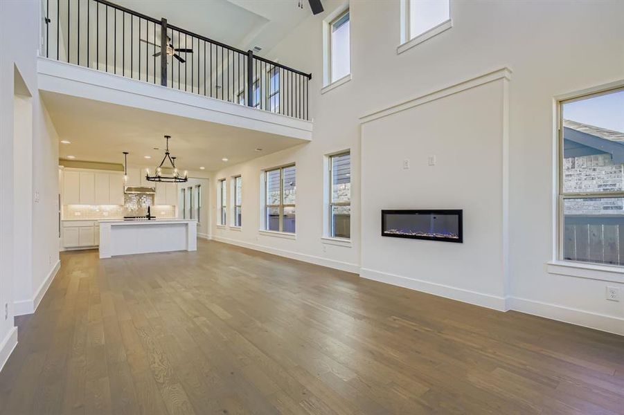 Unfurnished living room with a glass covered fireplace, dark wood-style floors, a ceiling fan, and a high ceiling Unfurnished living room with a glass covered fireplace, dark wood-style floors, a ceiling fan, and a high ceiling