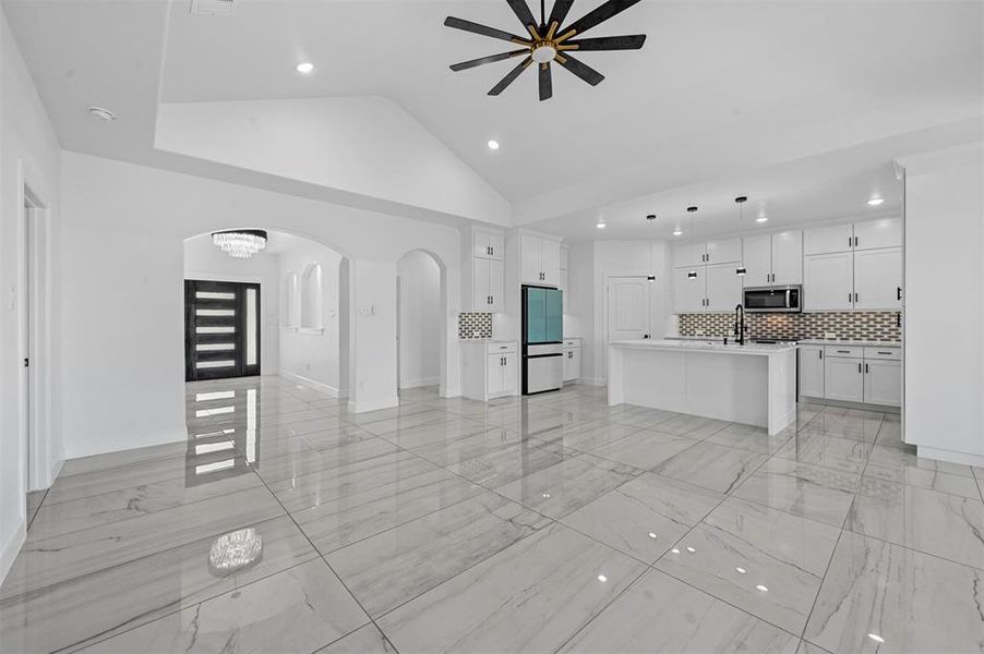 Unfurnished living room with high vaulted ceiling, sink, ceiling fan, and light tile patterned flooring