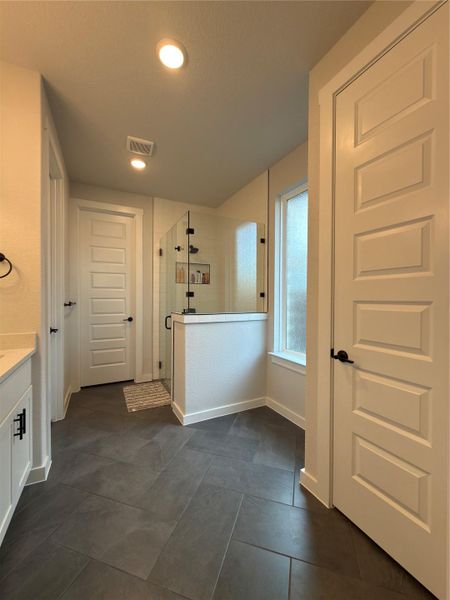 Spacious bathroom featuring large format tile flooring, a glass-enclosed shower with a built-in niche, and a window with privacy glass