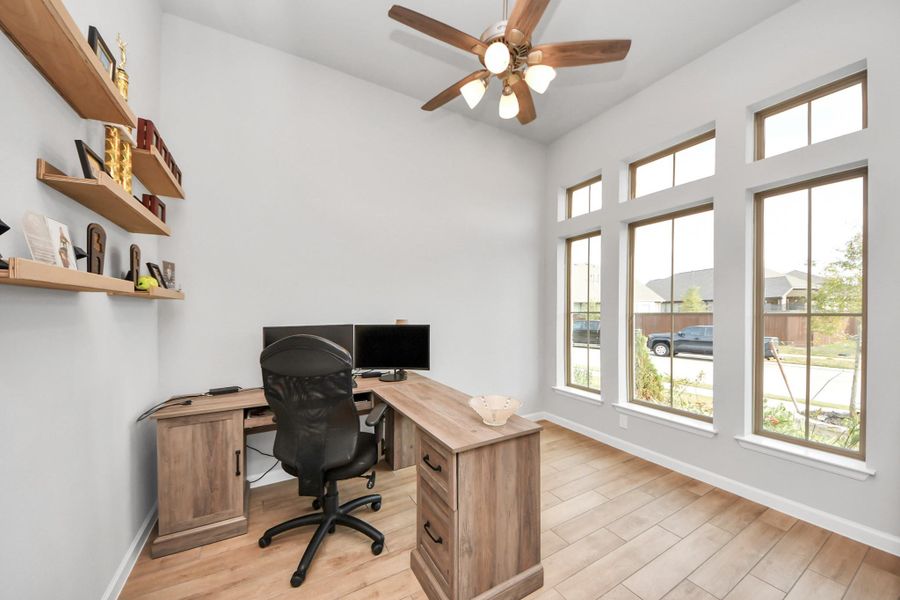 This photo showcases a bright home office with large windows, a ceiling fan, and wood flooring. It offers a functional and inviting workspace.