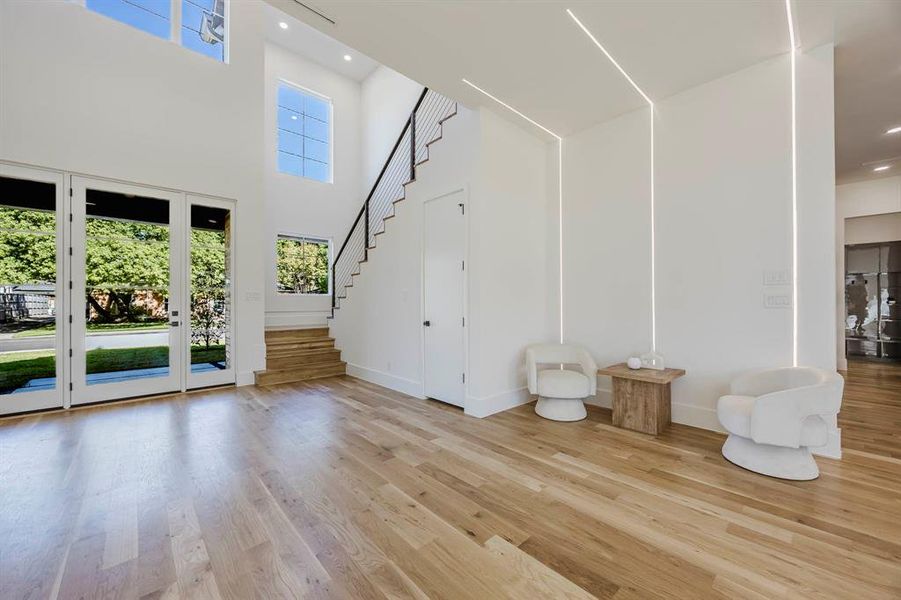 Unfurnished living room with light wood-type flooring, stairs, a towering ceiling, and recessed lighting Unfurnished living room with light wood-type flooring, stairs, a towering ceiling, and recessed lighting