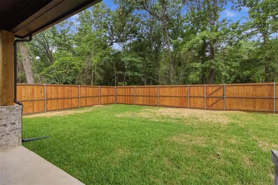 Expansive backyard featuring a wood fence, a patch of green grass, and mature trees beyond the fence line