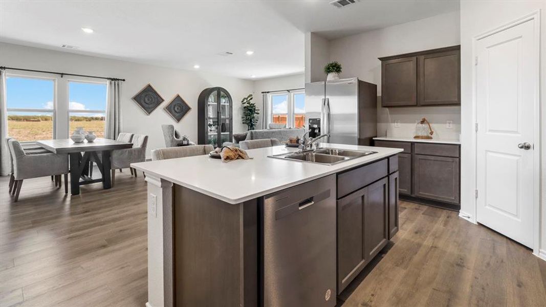 Kitchen featuring dark brown cabinets, stainless steel appliances, dark wood-style floors, open floor plan, and a center island with sink