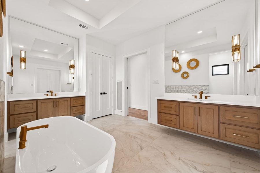 Primary 1 Ensuite: The spa-inspired primary bath creates a luxurious retreat featuring a freestanding soaking tub, designer tile accents and expansive flooring.Dual floating vanities with natural cabinetry and gold accents complete the elegant design!