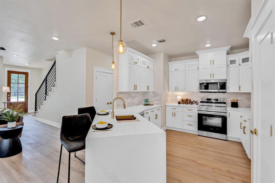 Kitchen with light hardwood / wood-style floors, kitchen peninsula, electric range, hanging light fixtures, and sink