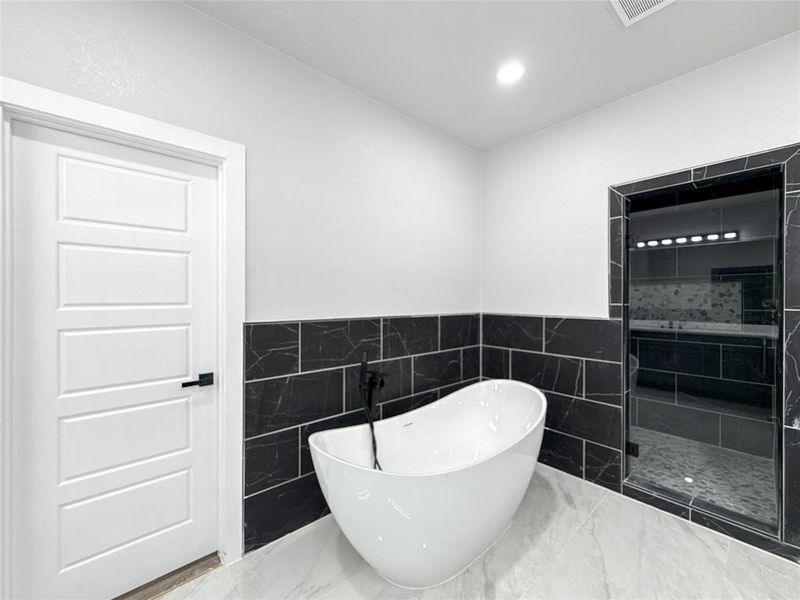 Full bathroom featuring tile walls, a stall shower, a freestanding bath, a wainscoted wall, and marble finish floors