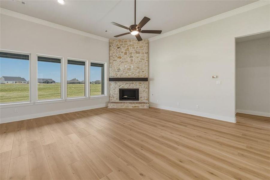 Spacious room featuring a stone-clad corner fireplace with a dark wood mantel, wood-finish flooring, a contemporary ceiling fan, and a wall of four large windows Spacious room featuring a stone-clad corner fireplace with a dark wood mantel, wood-finish flooring, a contemporary ceiling fan, and a wall of four large windows