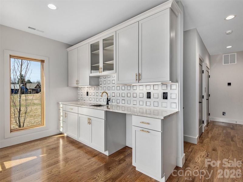 Lower-level entrance foyer featuring oak hardwood floors, Wolf cabinetry with sink, granite countertop, decorative tile backsplash, and access down the hall to the stairwell, elevator, third bedroom or office/study, and garage.