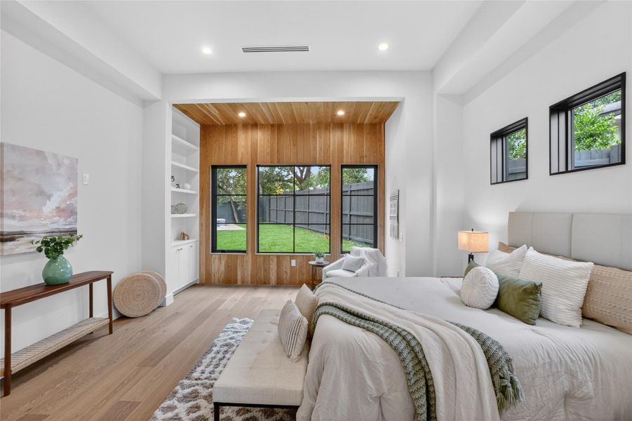 Elegant primary bedroom offering wood accents, built-in shelving, and a tranquil backyard view.
