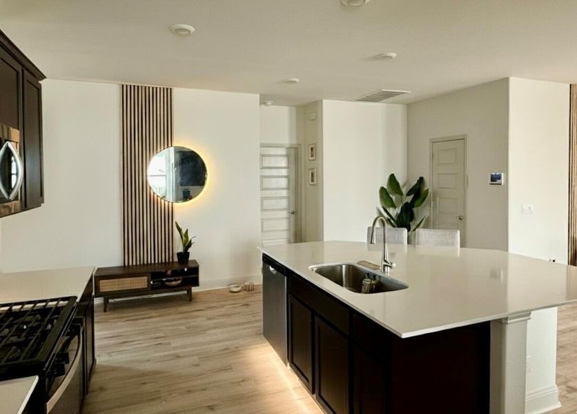 Kitchen featuring dark cabinetry, light wood-type flooring, an island with sink, appliances with stainless steel finishes, and light stone countertops
