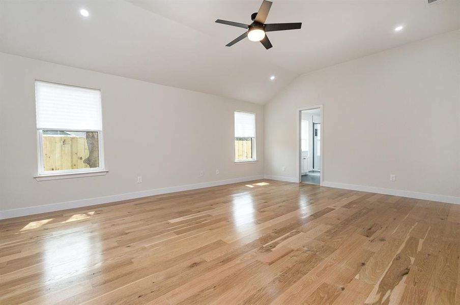 Empty room with a ceiling fan, lofted ceiling, light wood-style floors, and baseboards