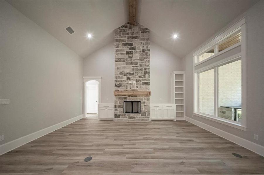 Unfurnished living room featuring light wood-type flooring, a stone fireplace, high vaulted ceiling, beam ceiling, and recessed lighting Unfurnished living room featuring light wood-type flooring, a stone fireplace, high vaulted ceiling, beam ceiling, and recessed lighting