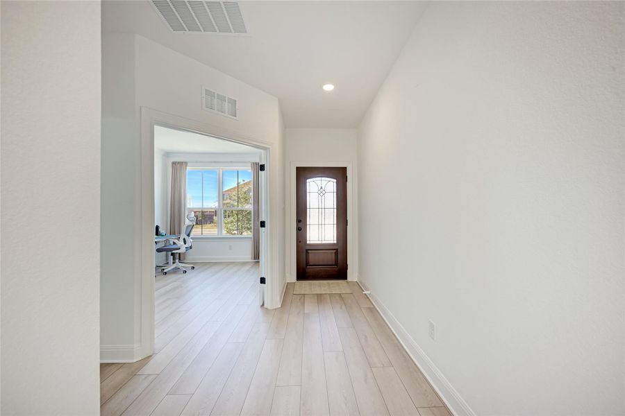 Entryway featuring light wood-finish flooring, a dark wood-paneled front door with decorative glass, recessed lighting, and white baseboards