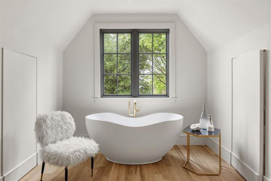 Bathroom featuring a freestanding soaking tub with brass fixtures, a transom window with dark muntins, light wood-finish flooring, and recessed storage Bathroom featuring a freestanding soaking tub with brass fixtures, a transom window with dark muntins, light wood-finish flooring, and recessed storage