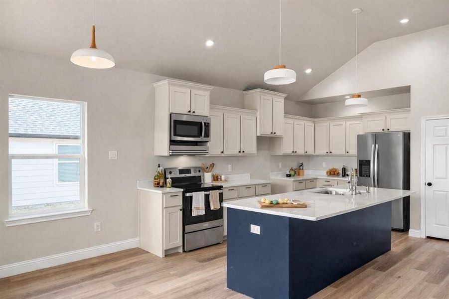 Dual tone kitchen featuring stainless steel appliances, an island with sink, light wood-style flooring, light stone counters, and vaulted ceiling