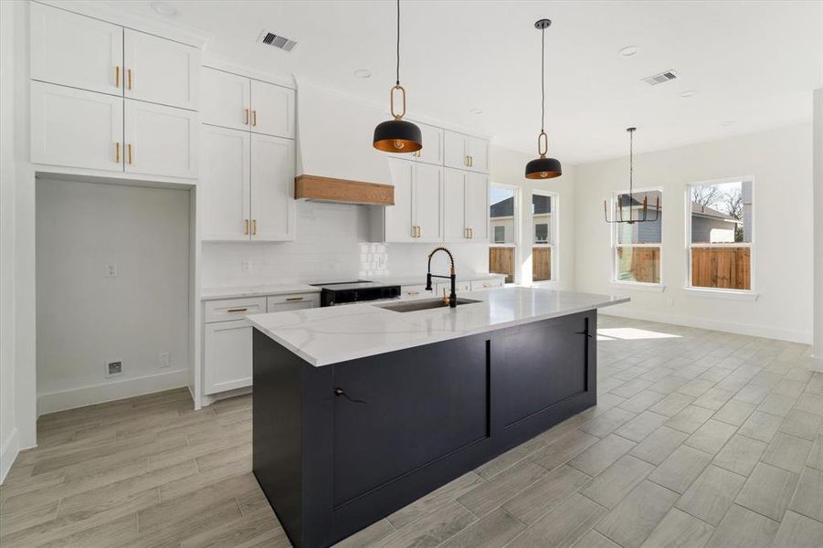 This stunning kitchen features custom white cabinetry, a custom vent hood, luxurious quartz countertops, and a huge island adorned with unique trim accents and two elegant pendant lights.