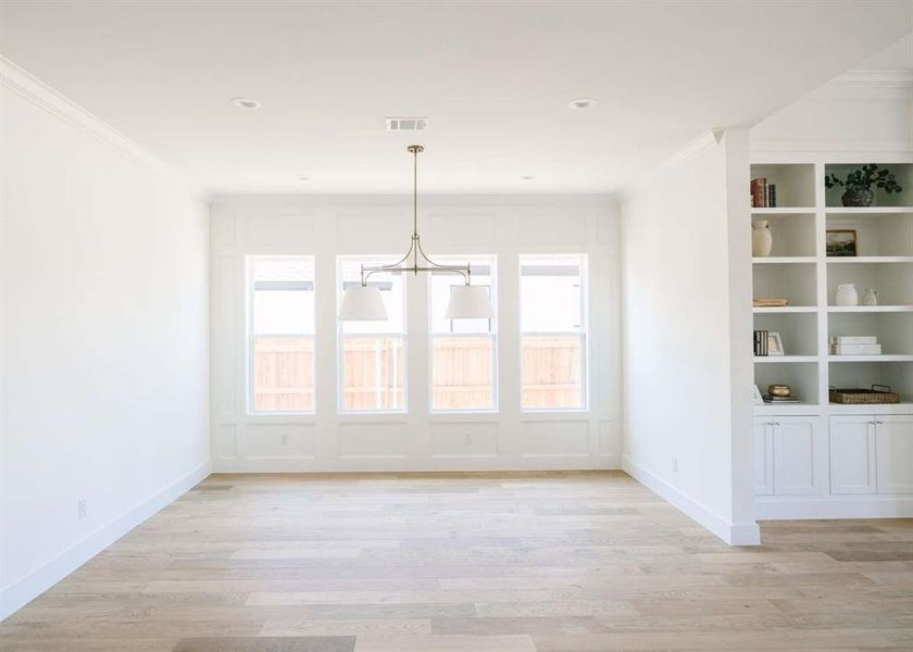 Unfurnished dining area with light hardwood / wood-style floors, ornamental molding, and a notable chandelier