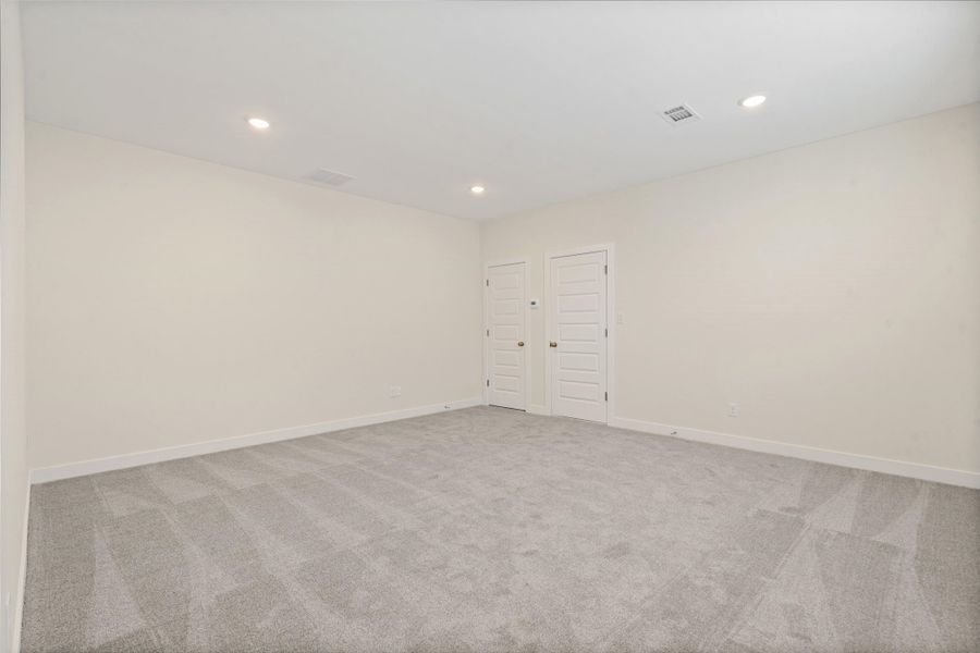 Spacious room with light neutral walls, recessed lighting, two paneled doors, and grey patterned carpeting Spacious room with light neutral walls, recessed lighting, two paneled doors, and grey patterned carpeting