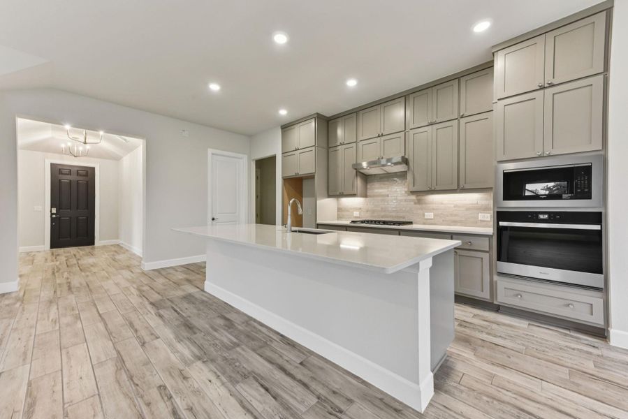 Kitchen featuring gray cabinets, appliances with stainless steel finishes, a kitchen island with sink, light stone countertops, and recessed lighting