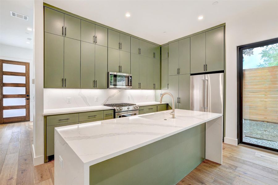 Kitchen with green cabinets, light wood-style floors, light stone countertops, high quality appliances, and recessed lighting Kitchen with green cabinets, light wood-style floors, light stone countertops, high quality appliances, and recessed lighting