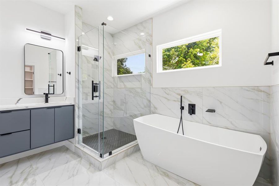 Contemporary bathroom featuring a freestanding soaking tub, frameless glass shower enclosure, a double vanity with grey cabinetry, and large format marble-look tile flooring and wall accents Contemporary bathroom featuring a freestanding soaking tub, frameless glass shower enclosure, a double vanity with grey cabinetry, and large format marble-look tile flooring and wall accents