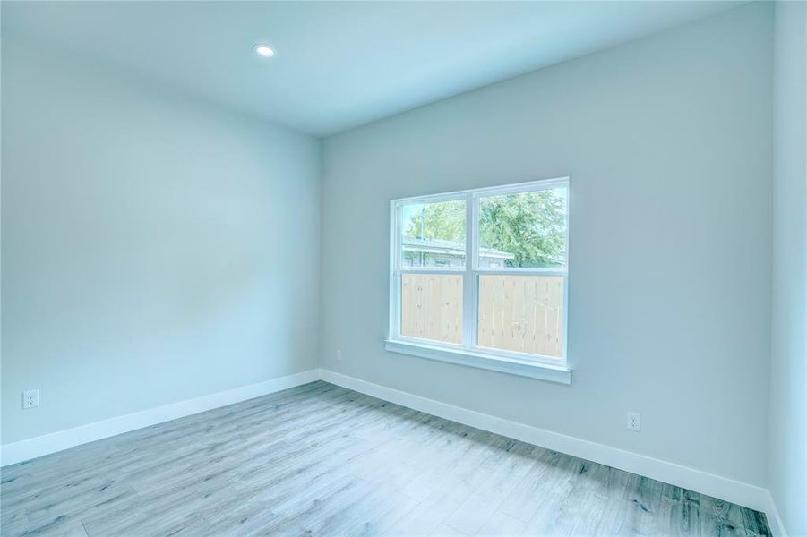 Interior room featuring a large window, light wood-finish flooring, recessed ceiling lighting, and white baseboards