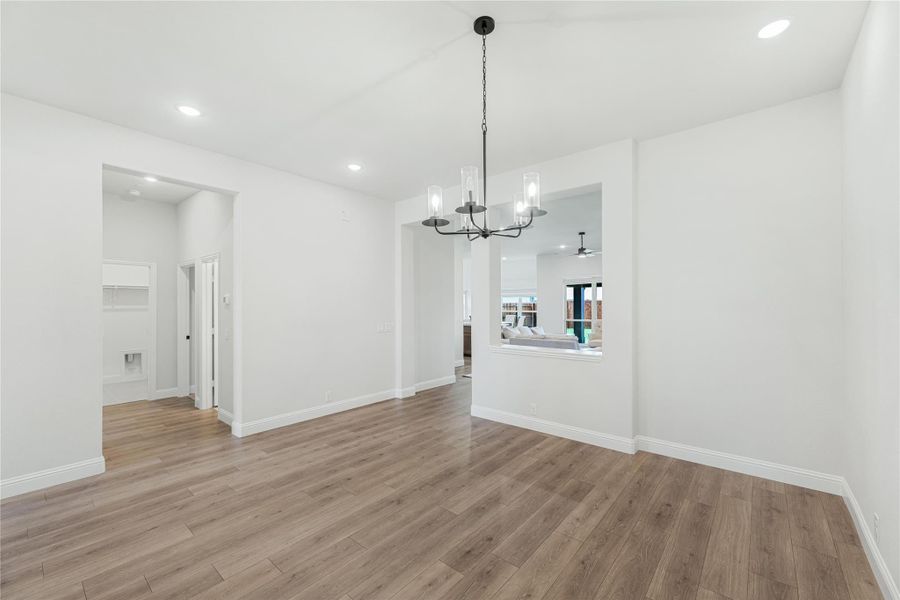 Empty dining room with wood-look floors, black chandelier, and open view to living area