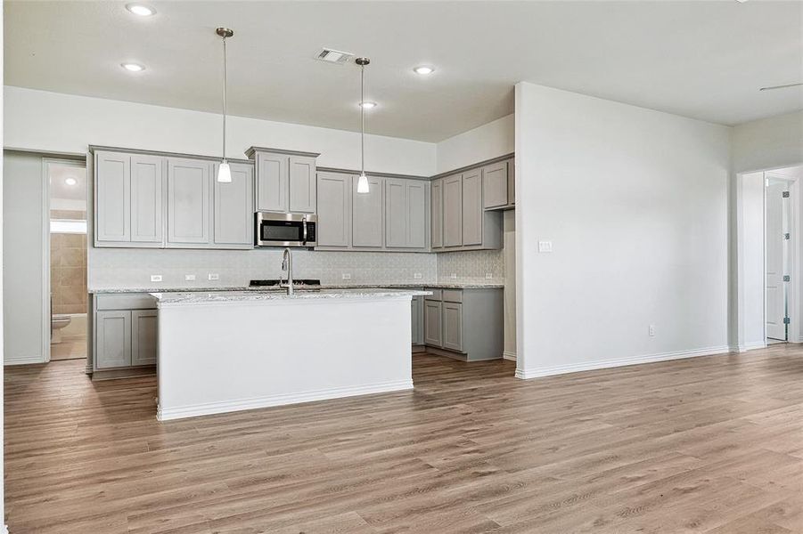 Kitchen with light hardwood / wood-style flooring, light stone counters, hanging light fixtures, and gray cabinetry