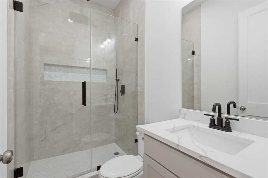 Modern bathroom featuring a frameless glass shower enclosure, large format tile shower surround, hexagon mosaic shower floor, and a recessed shower niche