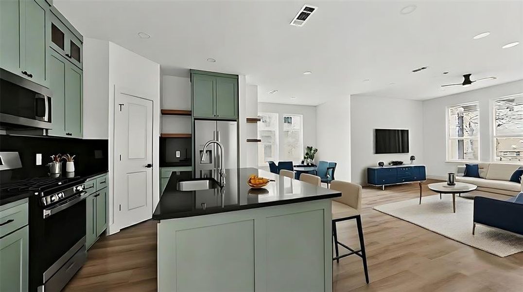 Kitchen featuring green cabinetry, stainless steel appliances, open floor plan, an island with sink, and dark wood finished floors