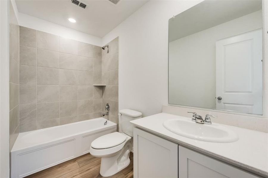 Full bathroom with tiled shower / bath, vanity, hardwood / wood-style flooring, and toilet