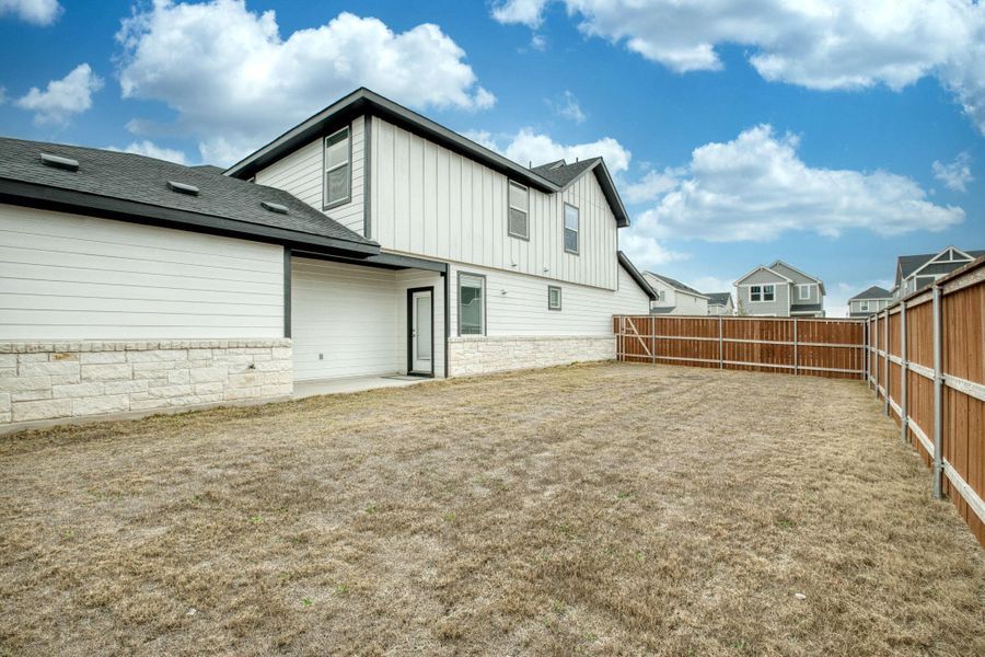 Back of house with a fenced backyard, a shingled roof, stone siding, board and batten siding, and a patio area