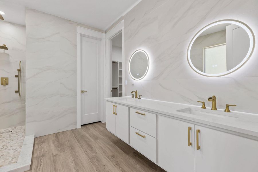 Full bath featuring double vanity, light wood finished floors, a marble finish shower, tile walls, and stone wall