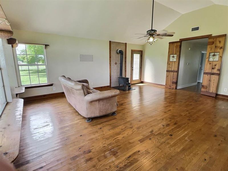 Living room with hardwood / wood-style floors, a wood stove, lofted ceiling, and ceiling fan