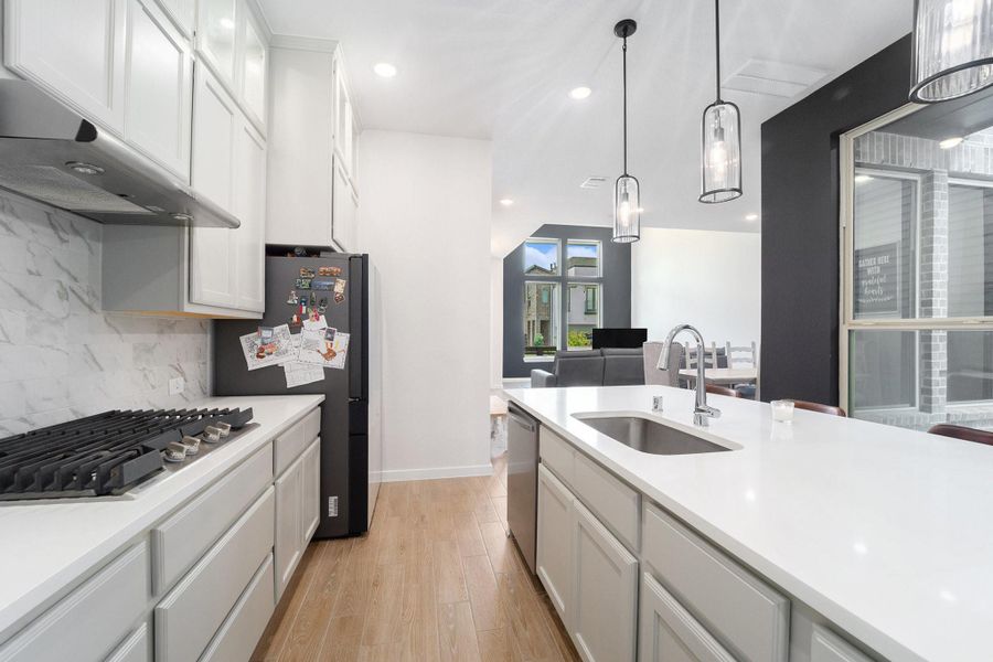 Open kitchen with quartz counters, gas cooktop, and pendant lighting overlooking the living room.