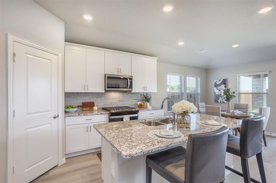 Kitchen with appliances with stainless steel finishes, white cabinets, backsplash, and recessed lighting Kitchen with appliances with stainless steel finishes, white cabinets, backsplash, and recessed lighting