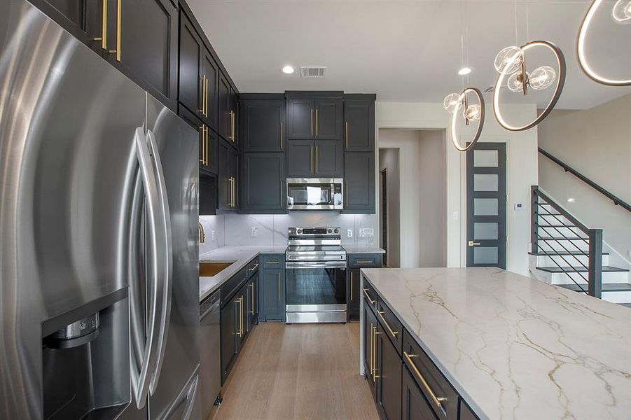 Kitchen with tasteful backsplash, light stone counters, stainless steel appliances, hardwood / wood-style floors, and hanging light fixtures