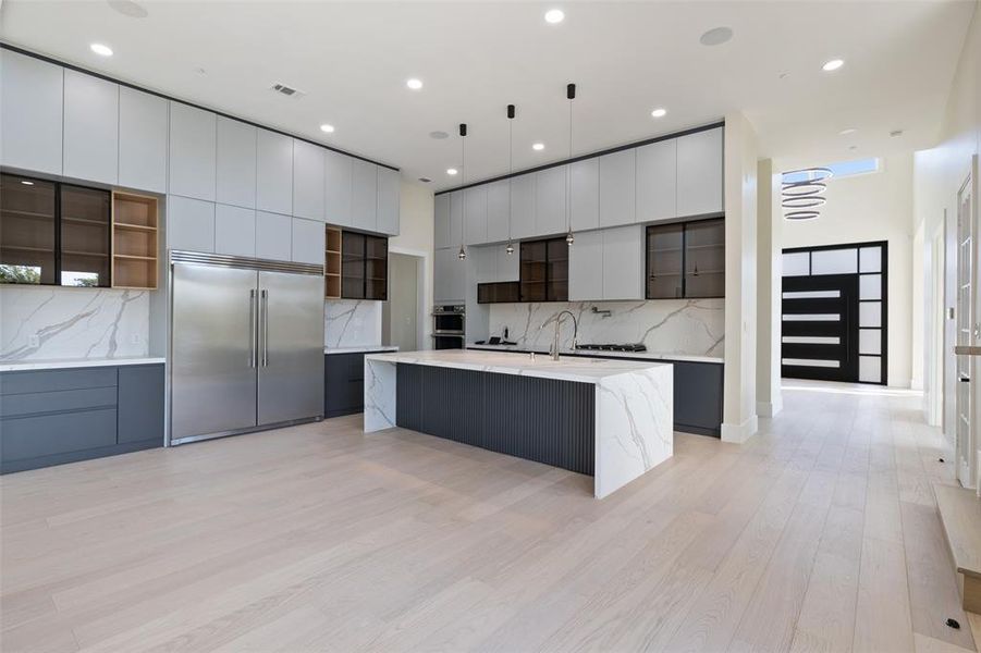 Kitchen with decorative backsplash, stainless steel appliances, light hardwood / wood-style floors, pendant lighting, and a large island