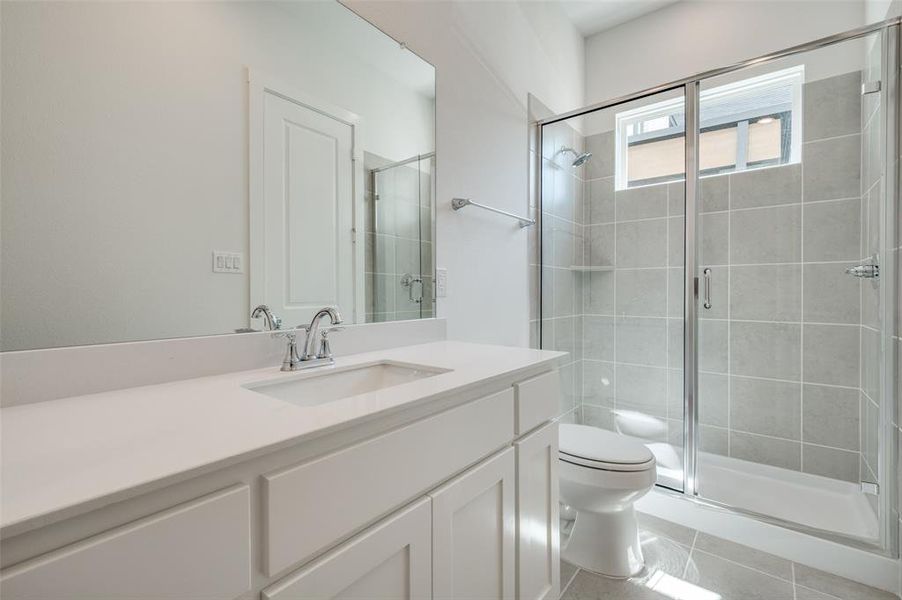 Bathroom with an enclosed shower, vanity, tile patterned floors, and toilet