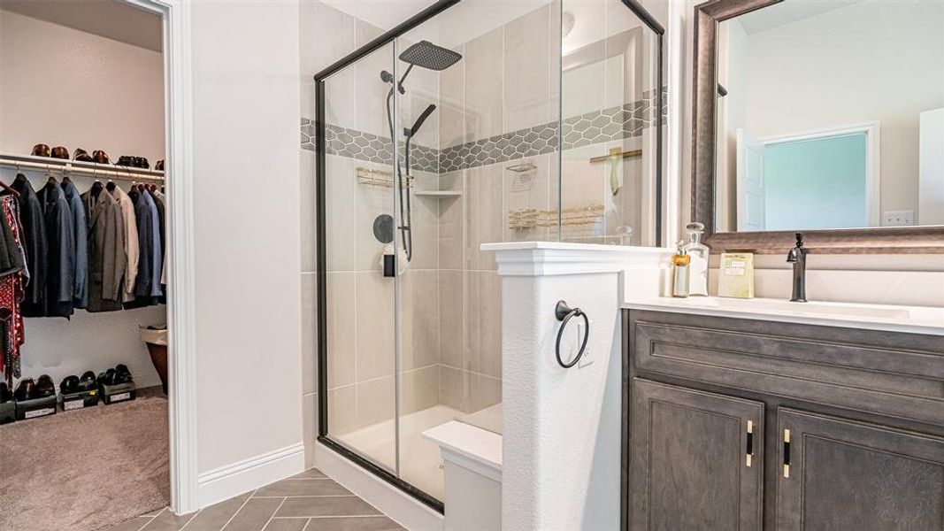 Bathroom featuring a glass-enclosed shower with a rainfall showerhead, a decorative tile band, and a built-in corner shelf
