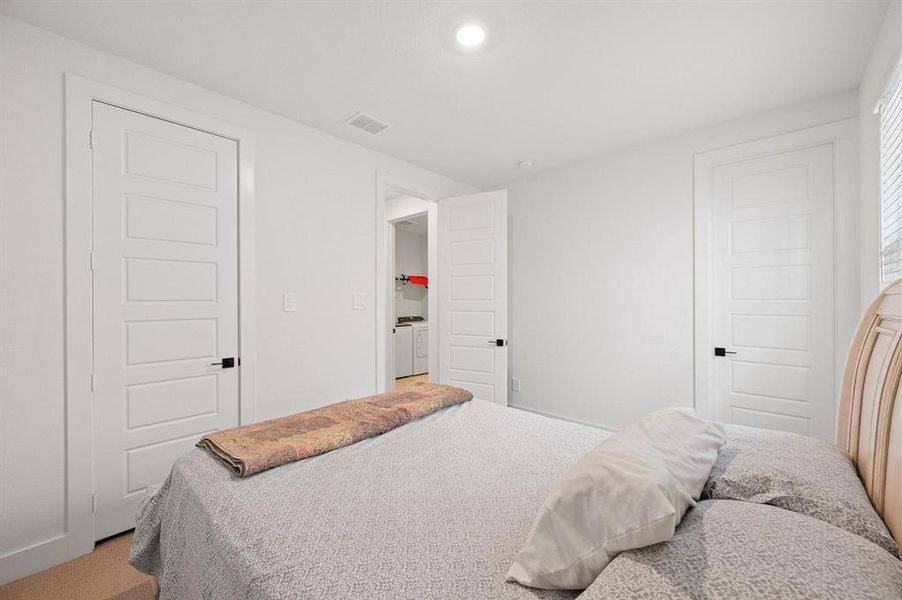 Bedroom featuring white walls, light-colored carpeting, recessed ceiling lighting, and multiple paneled doors with black hardware Bedroom featuring white walls, light-colored carpeting, recessed ceiling lighting, and multiple paneled doors with black hardware