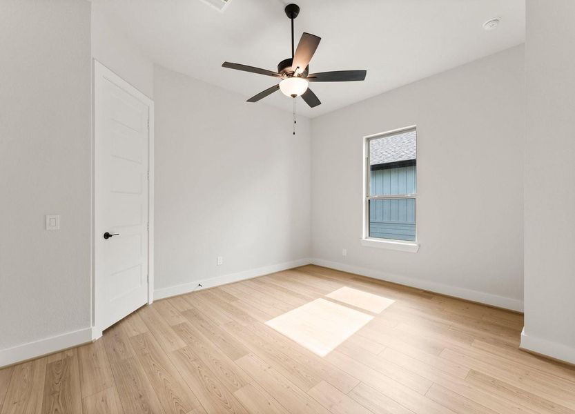 Bright, airy room with light wood flooring, a ceiling fan, and a single window for natural light. Perfect for a cozy bedroom or office space.