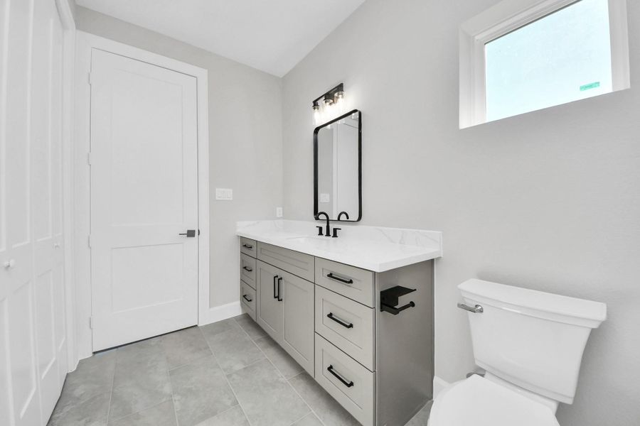 Stylish secondary bathroom featuring a quartz vanity, modern black fixtures, and a sleek tub-shower combo with marble-look tile surround.