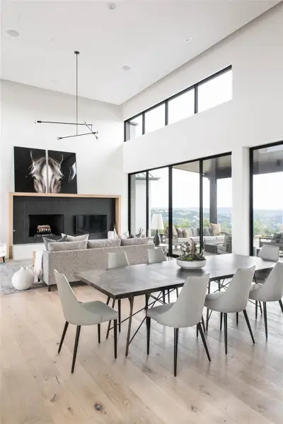 Dining area with light wood-style floors, a chandelier, a towering ceiling, recessed lighting, and a tiled fireplace