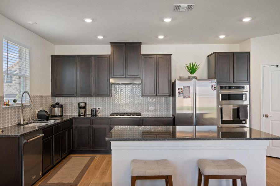 Kitchen with dark wood finish cabinetry, dark stone counters, a breakfast bar area, stainless steel appliances, and light wood-type flooring