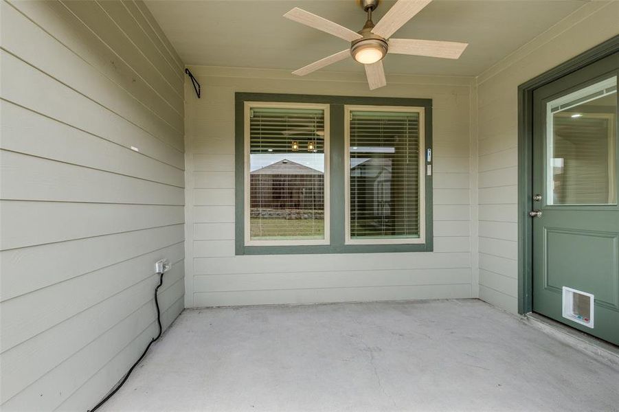 Covered patio featuring a ceiling fan with integrated lighting, concrete flooring, exterior siding, dual windows with blinds, and a green door with a partial glass insert Covered patio featuring a ceiling fan with integrated lighting, concrete flooring, exterior siding, dual windows with blinds, and a green door with a partial glass insert